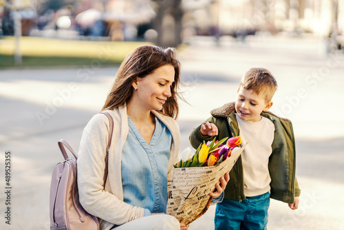 A little gentleman touching flowers while mother holding tulips in a park.