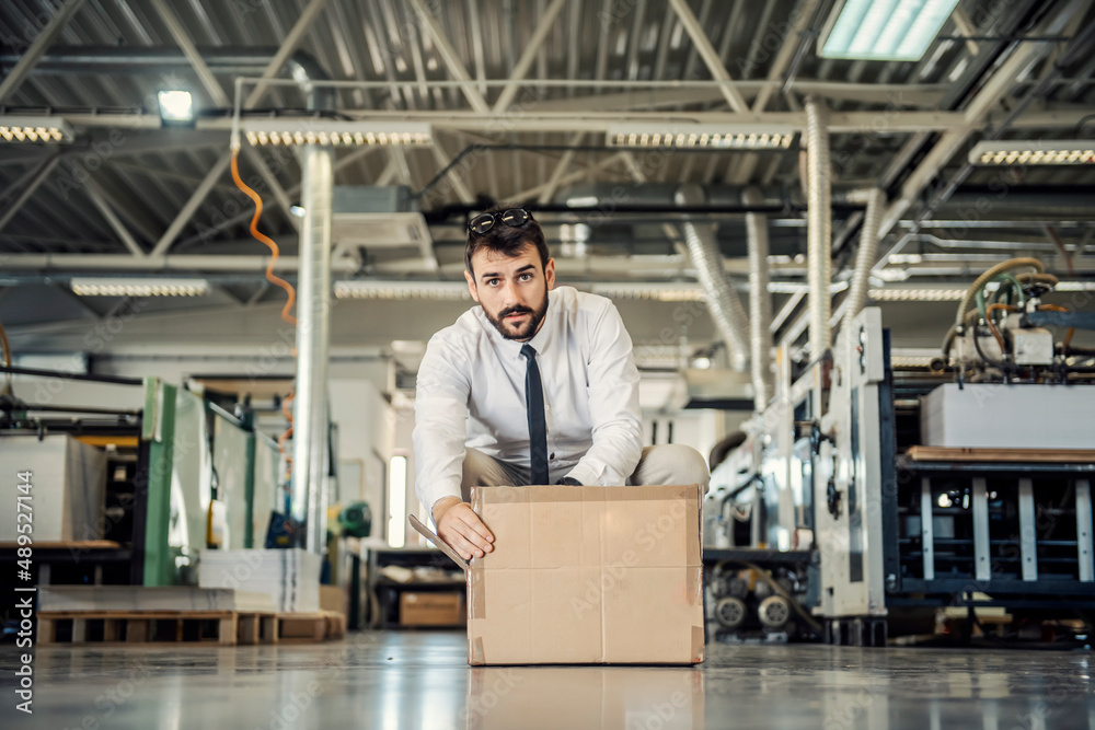 A manager crouching at printing shop and opening box.