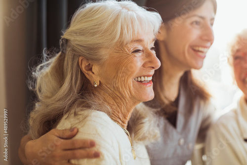 Happy elderly woman by female caregiver at nursing home photo