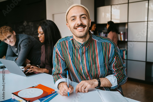 Portrait of smiling male student sitting with book at community college photo