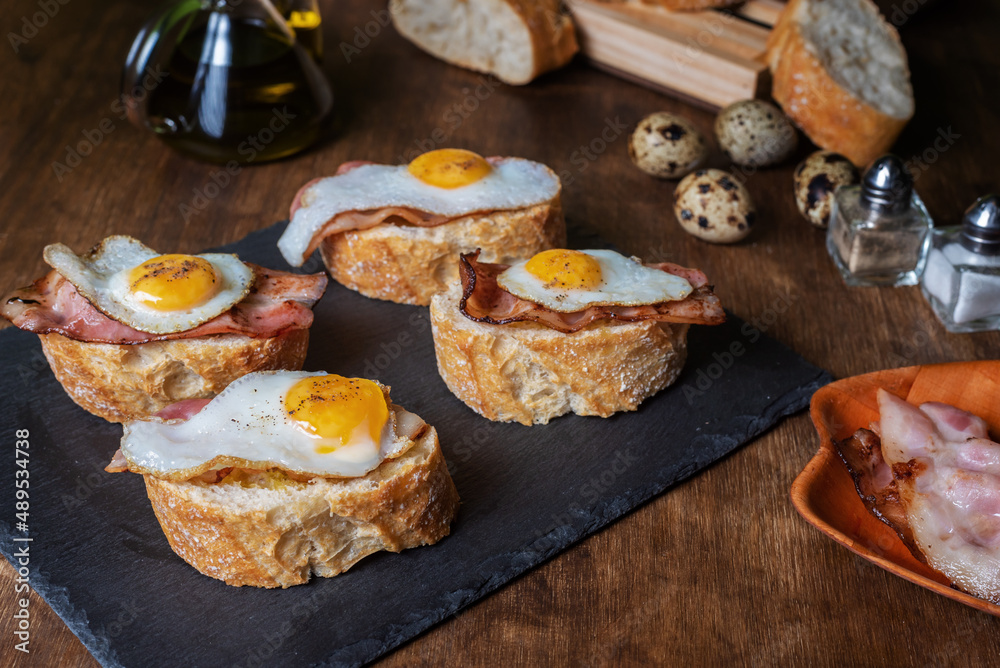 Slice of bread with bacon and grilled quail egg,on a wooden table.