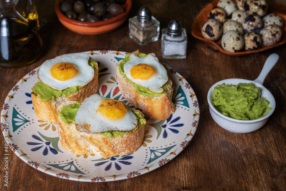 Slice of bread with avocado and grilled quail egg, on a wooden table.
