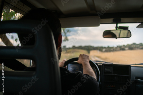 Young man driving a four wheel drive car in the countryside, driver inside the cabin of a car 4x4 , driving on an unsealed road, rural landscape in Spain photo