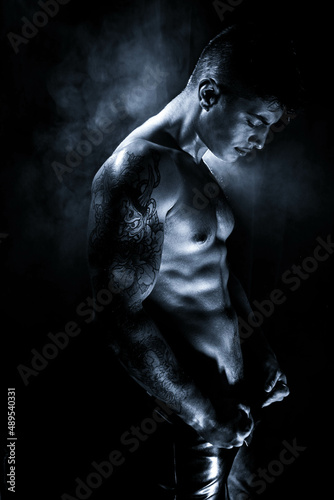 Moody low key portrait of attractive semi naked man with muscular body, pecs and defined abs