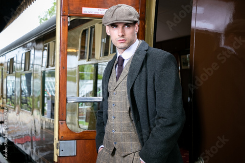 Handsome English male gangster at station leaving train looking at camera