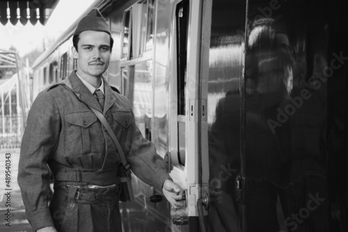Handsome male British soldier in WW2 vintage uniform at train station next to train, looking pensive