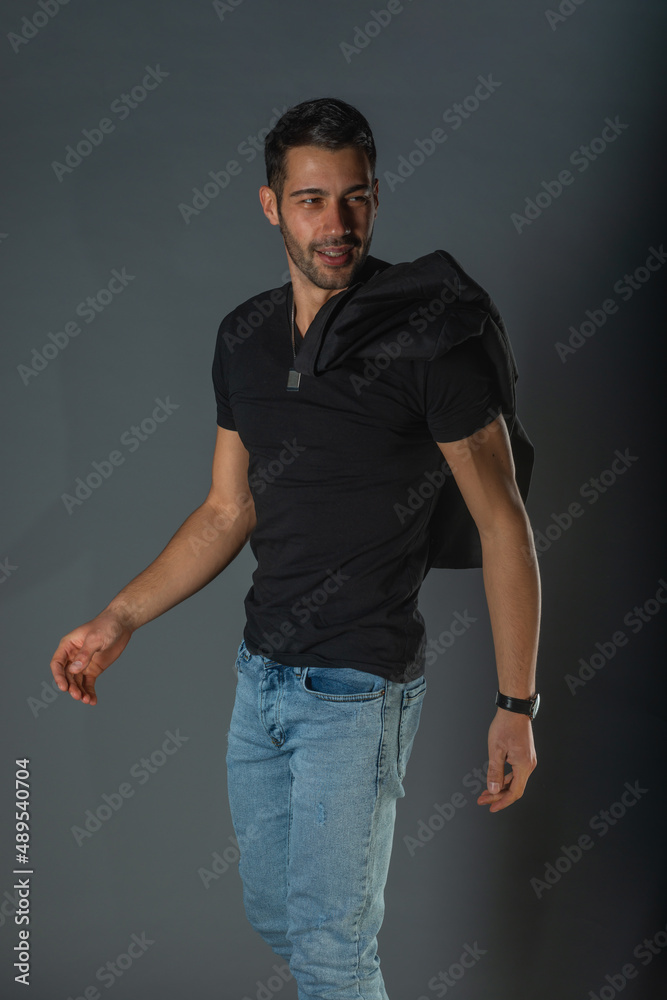 Strong muscular male model in jeans with black t-shirt holding his jacket over his shoulders Strong muscular male model in jeans with black t-shirt holding his jacket over his shoulders