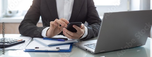 Female hands with mobile at office. Woman in formal wear scrolling apps on her smartphone at workplace, selected focus. photo