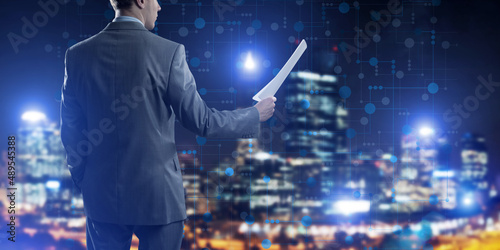 Rear view of businessman against night cityscape background and technology concept
