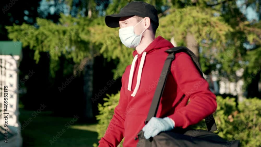 Asian delivery man in red uniform with face mask carrying bag of food delivering food to customer home during covid virus pandemic. He walking outdoor in village looking for customer home address Asian delivery man in red uniform with face mask carrying bag of food delivering food to customer home during covid virus pandemic. He walking outdoor in village looking for customer home address