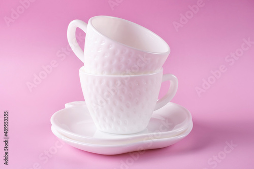 Two beautiful white cups in the shape of strawberries and two saucers on a pink background. Empty dishes.