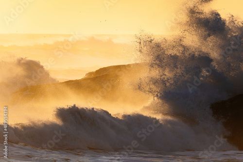 Stock photo of strong waves breaking against rocks on a beach in Iceland at sunset. 
