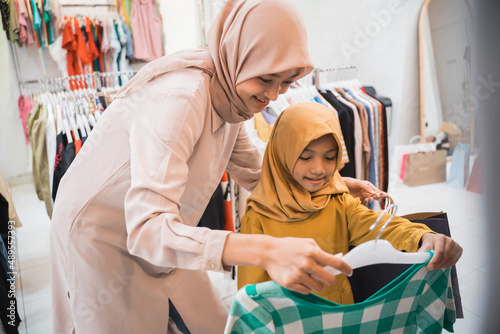 muslim mother choosing shirt with daughter during shopping at fashion shop