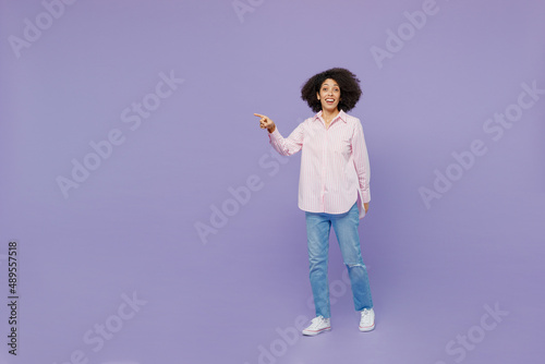 Full body smiling fun young woman of African American ethnicity 20s wear pink striped shirt walk go point finger aside on workspace isolated on plain pastel light purple background studio portrait © ViDi Studio