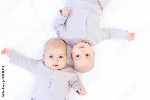 two newborns a twin baby a girl in a cotton suit on a white bed at home are lying and smiling