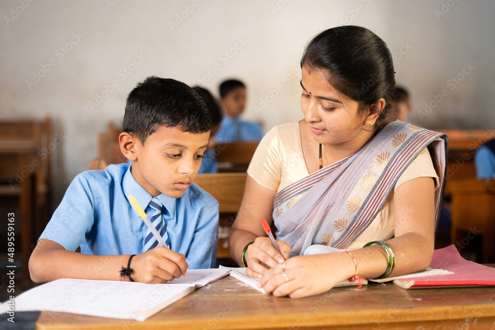 Teacher in classroom helping kid for studying at desk - concept of personal care, mentorship and coaching Teacher in classroom helping kid for studying at desk - concept of personal care, mentorship and coaching