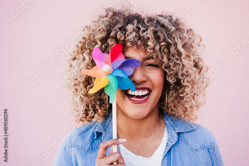 beautiful happy hispanic woman with afro hair holding colorful pinwheel. pink background,wind energy