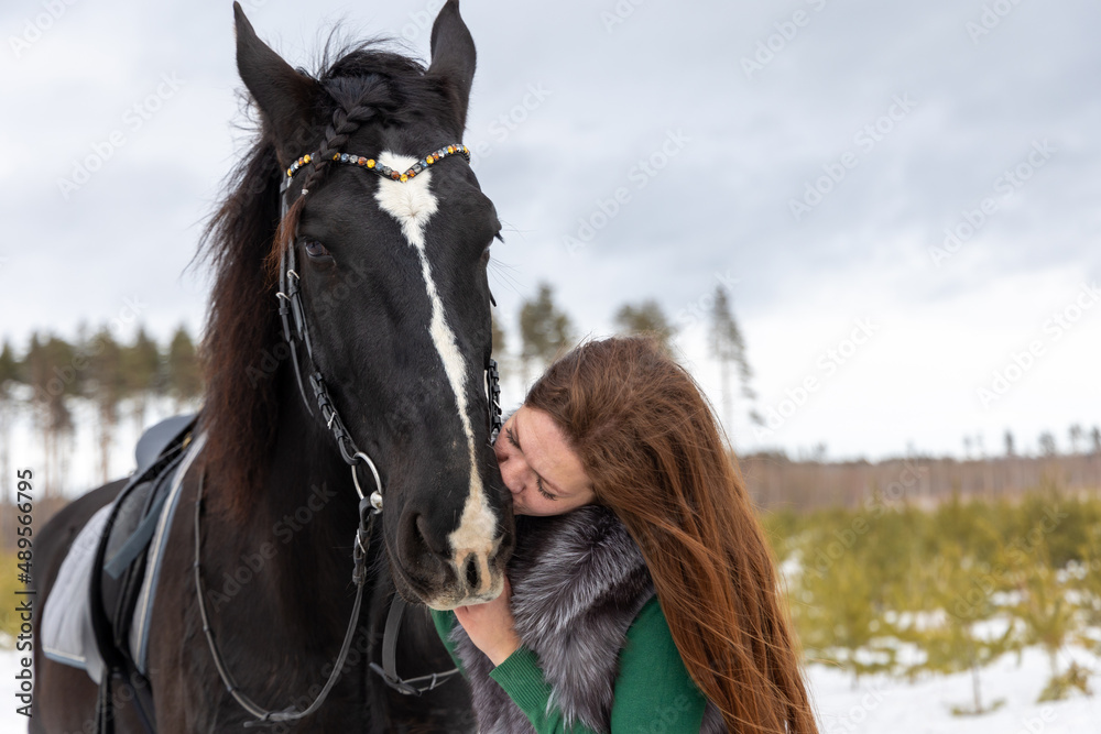 Obraz premium Girl on a black horse. Walk with a horse through the countryside. Russia. Lipetsk 20.02.2022