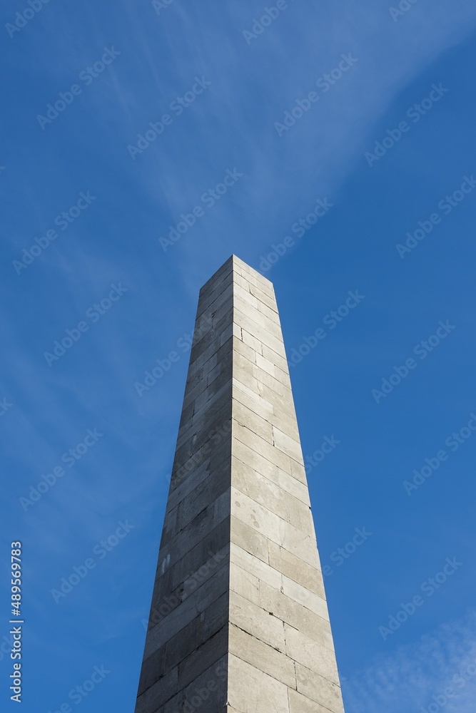 Photograph of the Monument to Victims. In background with beautiful blue sky and tiny clouds. Beautiful sunny weather. Flying plane.