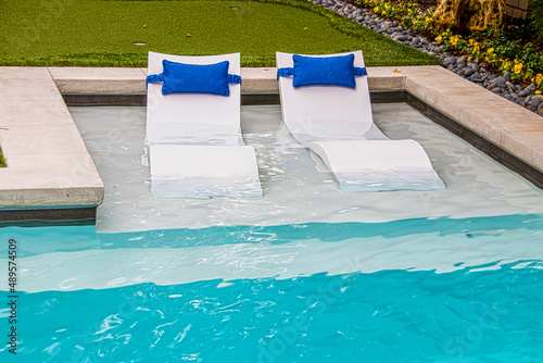 Photography Comfy white loungers in shallow end of refreshing blue swimming pool in yard wit