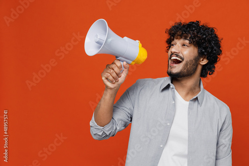 Fotomurale Jubilant overjoyed excited vivid young bearded Indian man 20s years old wears blue shirt hold scream in megaphone announces discounts sale Hurry up isolated on plain orange background studio portrait