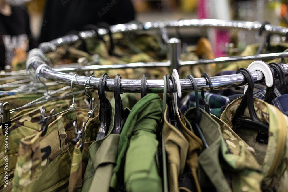 Department in the men's military clothing store. Camouflage uniforms hang on hangers in a military store