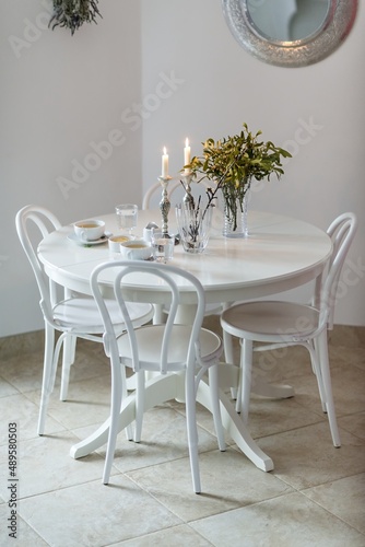 christmas welfare, table with chairs and Christmas tablecloth, mistletoe, lighted candles and a cup of tea, in the background a mirror with flowers © Mario
