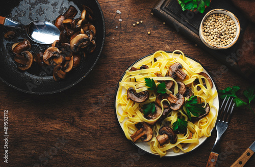 Tasty fettuccine pasta with mushrooms served on plate with greens and spice on rustic wooden kitchen table background  top view. Healthy vegetarian cooking and eating. Italian food concept