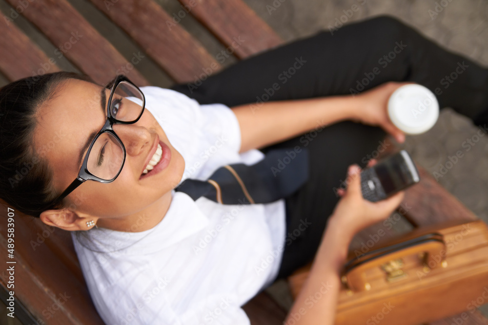 I learn, what is your superpower. A beautiful young woman winking at the camera while sitting on a bench with her cellphone, coffee and satchel. I learn, what is your superpower. A beautiful young woman winking at the camera while sitting on a bench with her cellphone, coffee and satchel.