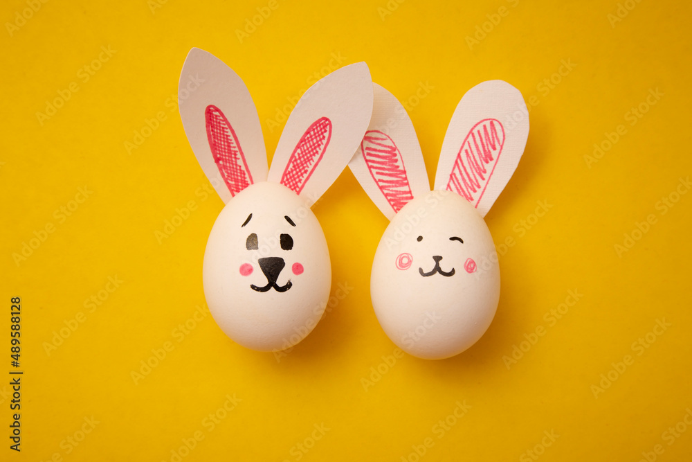 Photo of food for Happy Easter. Chicken eggs with cute bunny faces and rabbit ears on a yellow background. Preparation for the holiday. Greeting card for Easter holiday. Photo of food for Happy Easter. Chicken eggs with cute bunny faces and rabbit ears on a yellow background. Preparation for the holiday. Greeting card for Easter holiday.
