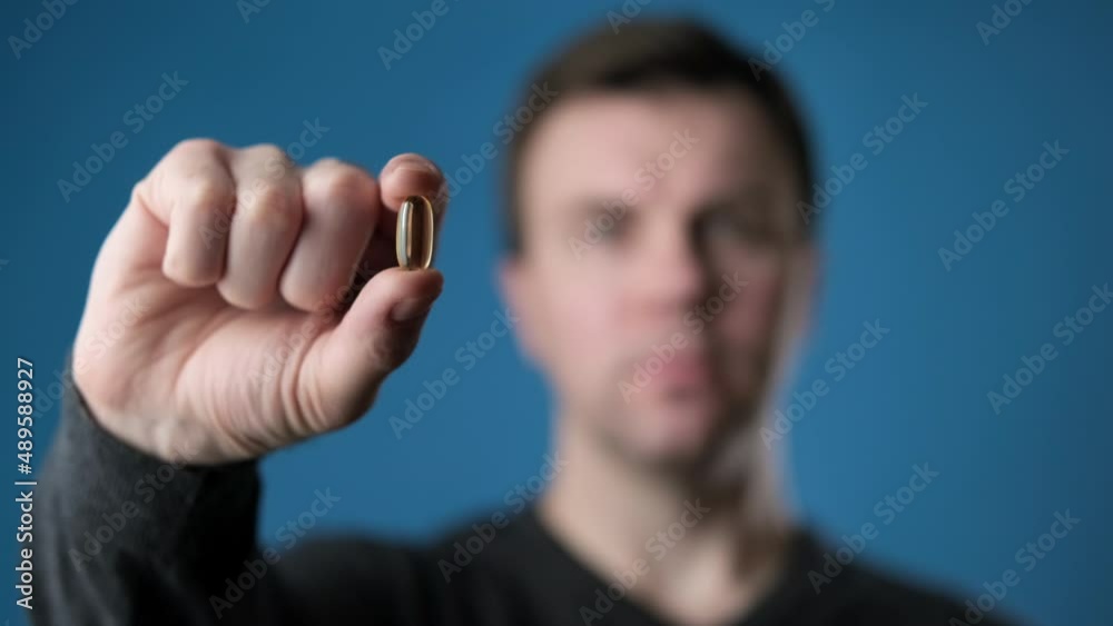 Young man showing vitamin pill. Medicine concept. Male holding pill in hand. Blurred man preparing to drink pill with omega-3. 4K, UHD Young man showing vitamin pill. Medicine concept. Male holding pill in hand. Blurred man preparing to drink pill with omega-3. 4K, UHD