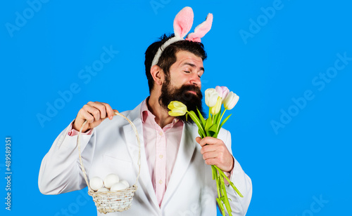 Easter celebration. Bearded man with basket eggs and tulips. Egg hunt. Rabbit ears. Spring Holidays.