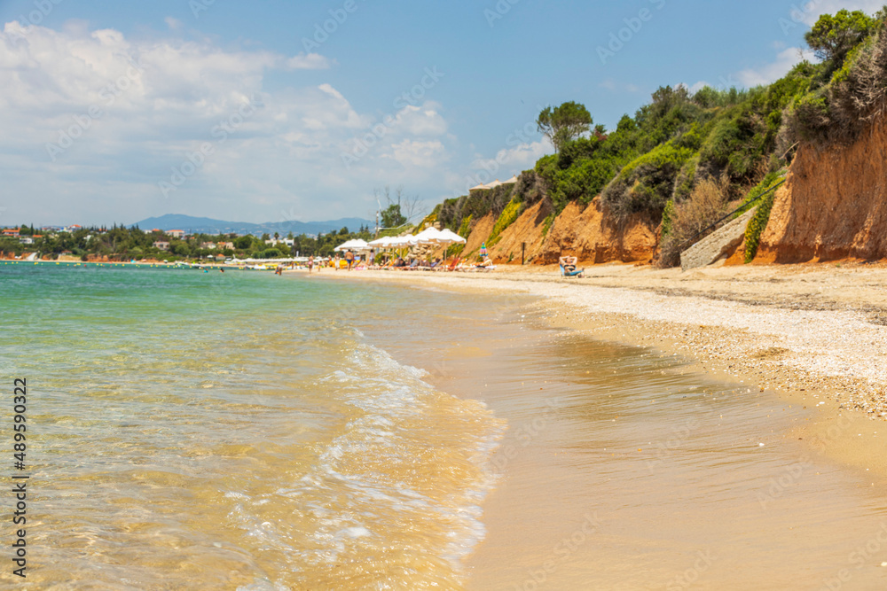 Beautiful view of sandy beach of Mediterranean Sea with people relaxing on bright summer day. Greece.