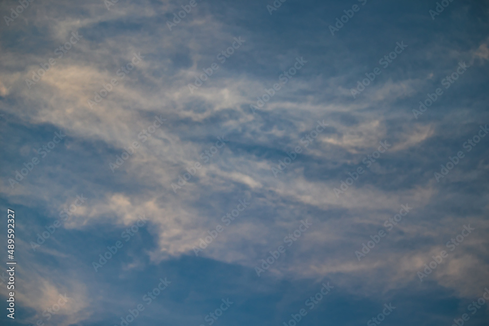Veil of thin clouds shaded in orange, floating under a blue sky.