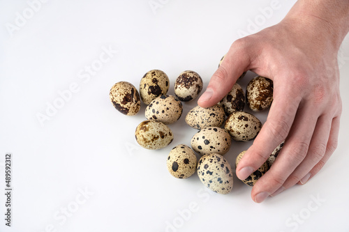 man's hand lies on fresh quail eggs on white background. The concept of healthy eating and home cooking. Poultry farming, home farm
