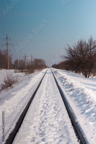 Railway going to the perspective. Powerlines and trees nearby. Snowy winter landscape
