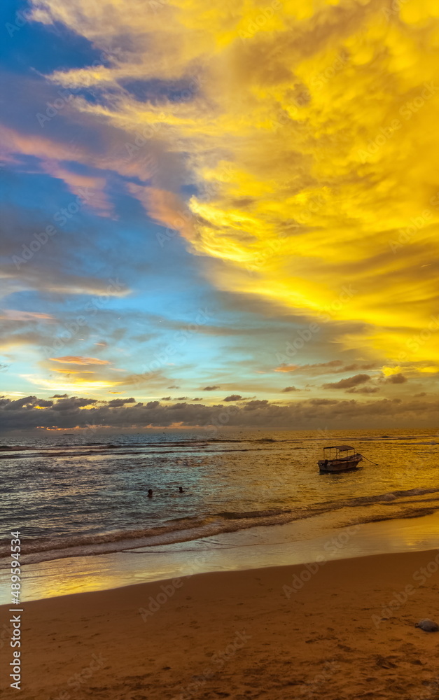 Summer evening landscape on the sandy shore of the Indian Ocean with boats against the sky with clouds illuminated by the sun at sunset. Sri Lanka