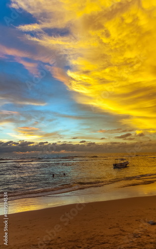 Summer evening landscape on the sandy shore of the Indian Ocean with boats against the sky with clouds illuminated by the sun at sunset. Sri Lanka