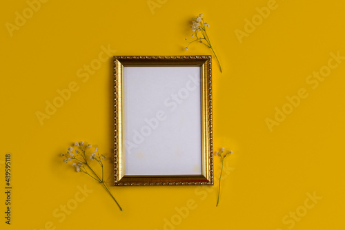 Flat lay with empty golden photo frame and gypsophilia flowers on yellow background. photo