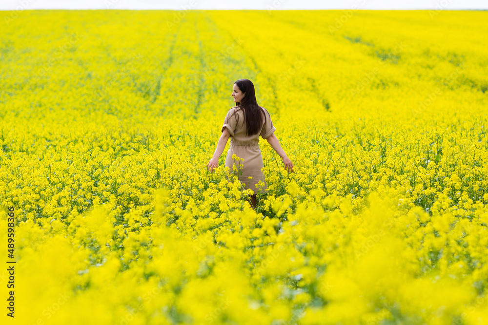 Happy woman walks run along yellow field rapeseed, hands raised to side enjoys nature. Happy woman walks run along yellow field rapeseed, hands raised to side enjoys nature.