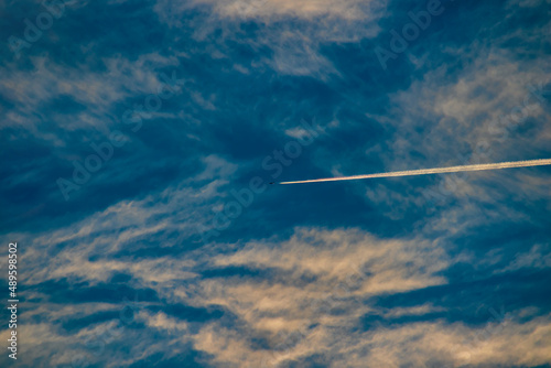 silhouette of a jet leaving a trail of steam lit by sunlight, under an impressionistic blue sky.
