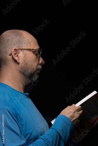 Portrait of a bearded, bald man reading a book against black background. photo