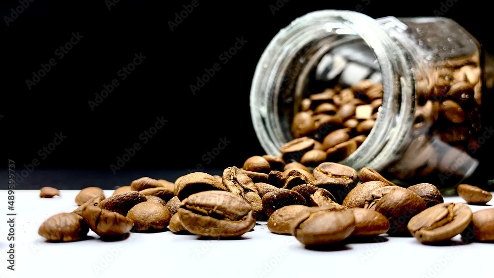 Whole raw coffee beans poured out of a jar on a table on a black background Whole raw coffee beans poured out of a jar on a table on a black background