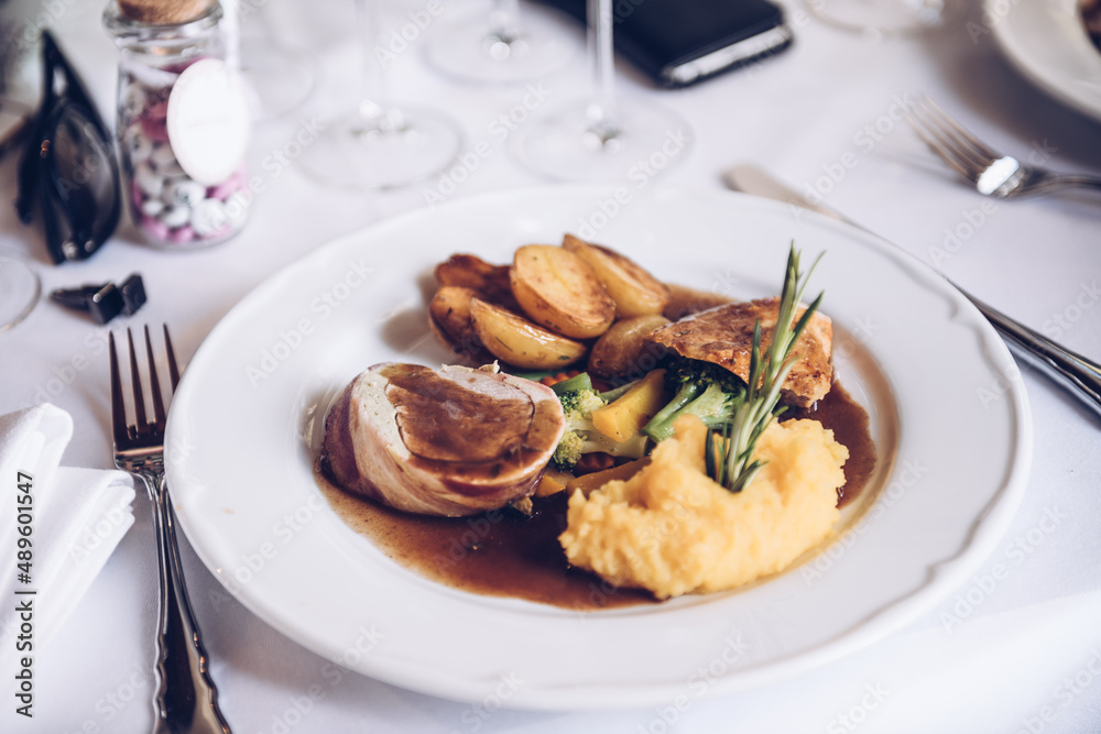 Weißer Teller auf weißem Tischtuch mit Schweinsmedalions und Kartoffeln als Beilage.