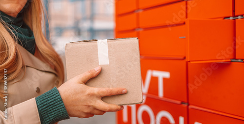 Young caucasian woman using automated self service post terminal machine or locker to deposit the parcel for storage photo