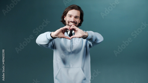 An adult man is showing a heart from his hands and looking at the camera