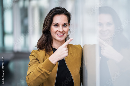 happy smiling casual business lady pointing her finger to a white wall at a modern bright white lobby 