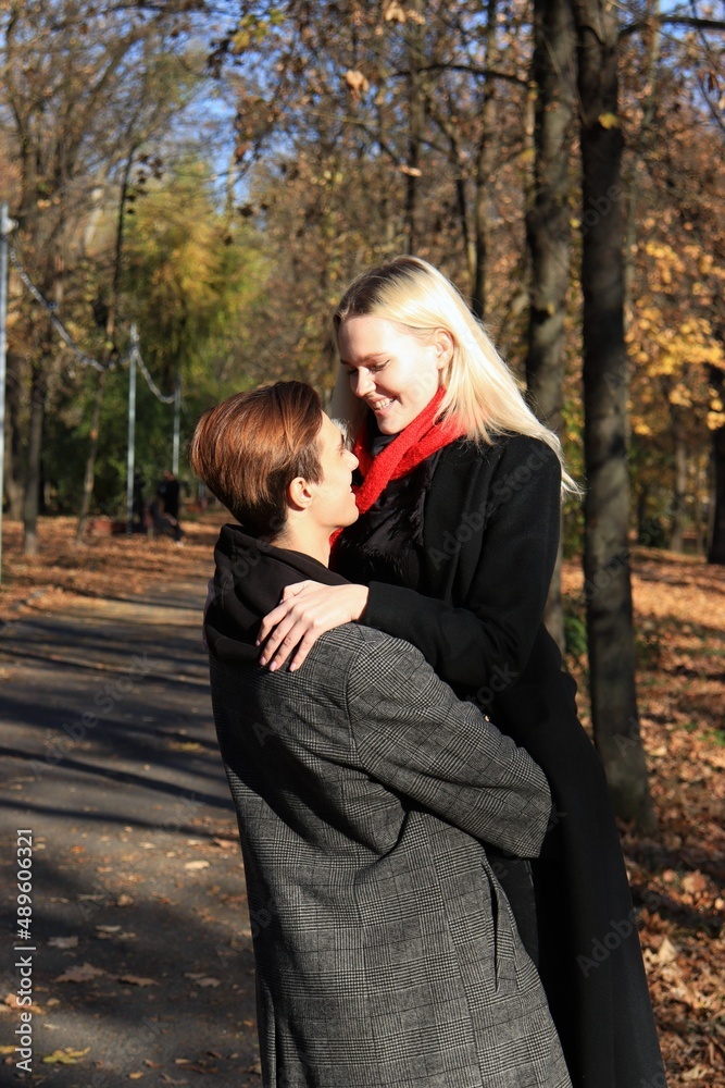 Fototapeta premium A young couple are standing in a park or forest. A couple in love - a blonde girl and guy.The guy holds the girl in his arms, they look at each other. Joint walk.Romantic relationship. Valentine's Day