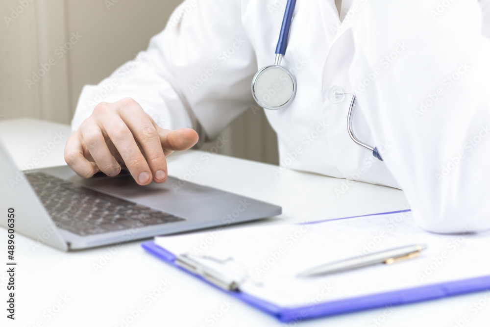 Male doctor hands using tablet computer. Physician in white coat with stethoscope sitting at desk. Professional medical diagnosis and treatment in clinic