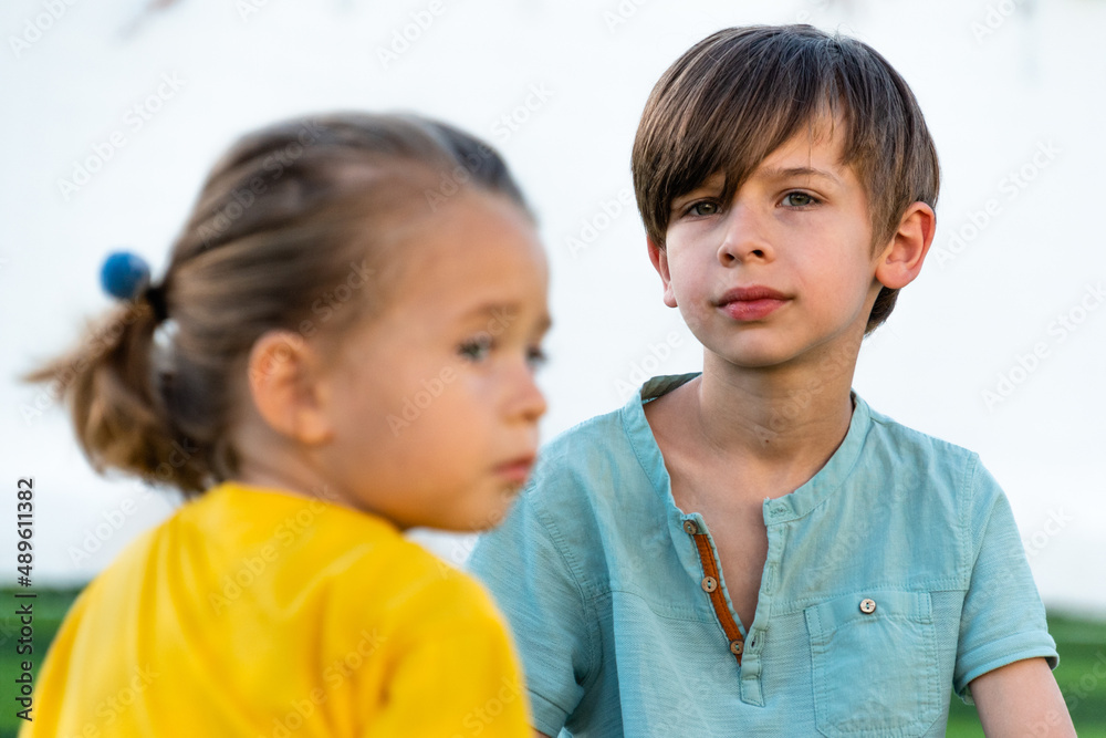 Pensive boy sitting near girl and looking to camera while spending time together on green lawn during break from football game Pensive boy sitting near girl and looking to camera while spending time together on green lawn during break from football game